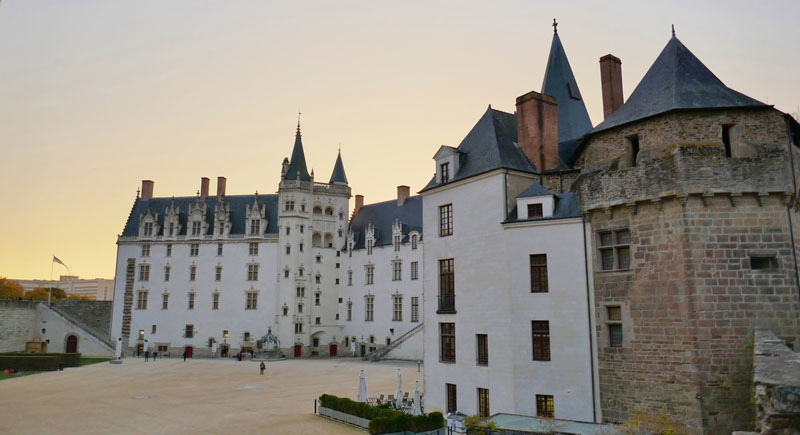 Enorme castillo con torres puntiagudas en su tejado de pizarra sobre paredes blancas perforadas por torres en Nantes