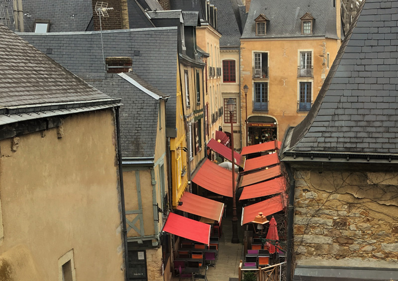 Vista desde una ventana alta de una calle adoquinada en Le Mans, coloridos toldos cubren restaurantes