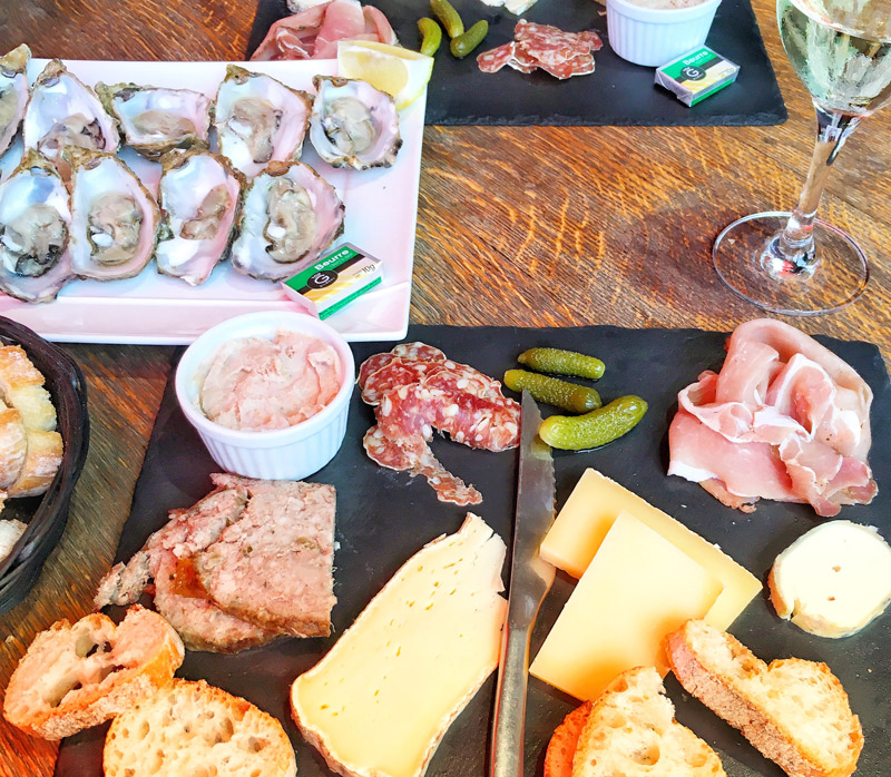 Bandeja de pizarra de ostras, queso, carnes, pan y una copa de vino - un almuerzo típico francés