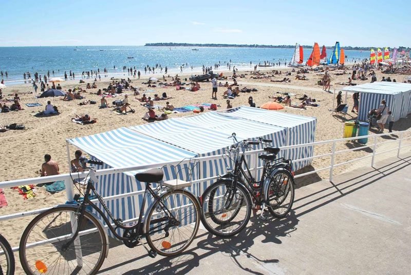 Una larga playa de arena dorada bajo un cielo azul, bicicletas apoyadas contra barandillas