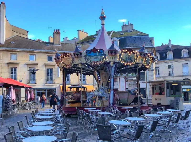 Carrusel al anochecer en una plaza adoquinada bordeada de restaurantes, mesas y sillas en el exterior, Dijon, Bugundy