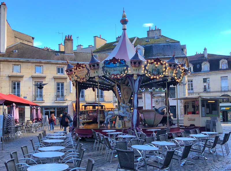 Plaza adoquinada con un carrusel en el centro, llena de edificios antiguos en Dijon, Borgoña