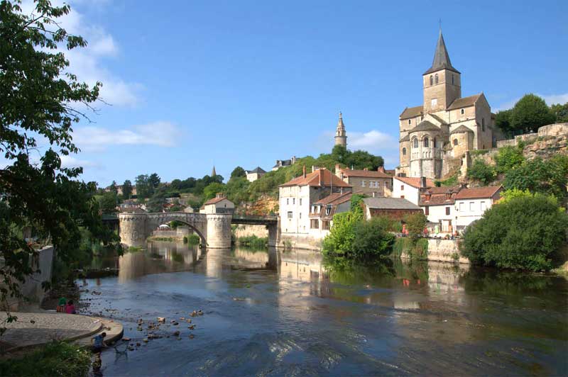 Puente de piedra sobre un río, pueblo de antiguos edificios de piedra coronado por una abadía al lado del río