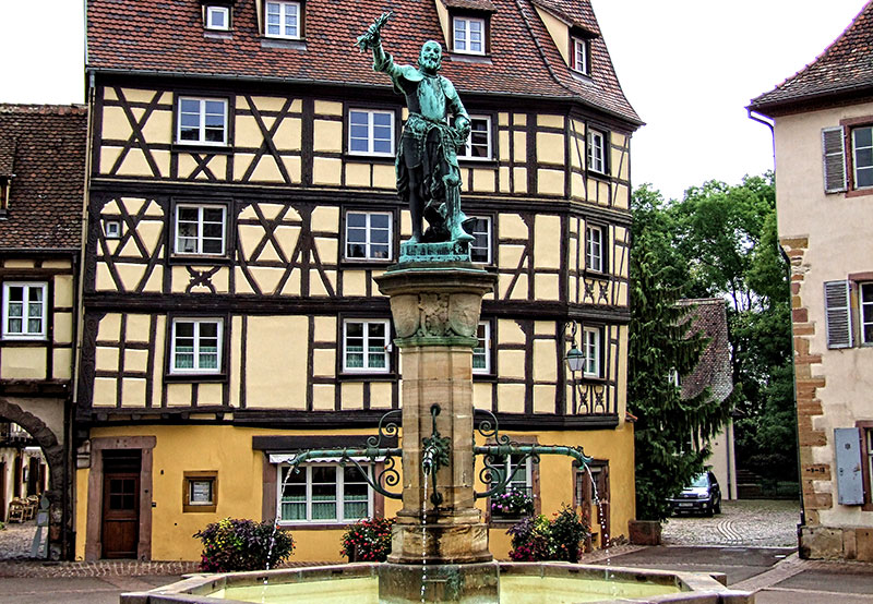 Fuente Schwendi, Colmar coronada por una estatua de un hombre que sostiene un racimo de uvas