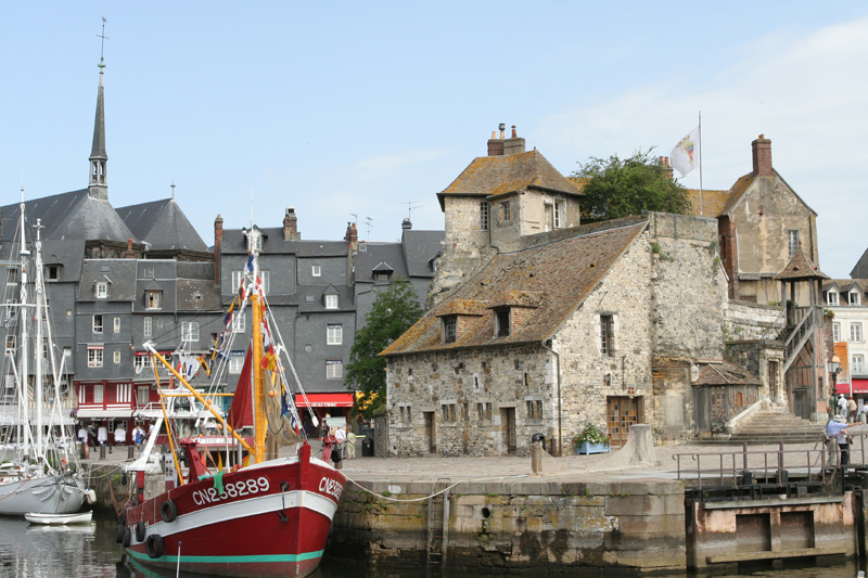 Barco en un pequeño puerto, antiguos edificios de piedra al fondo en Honfleur