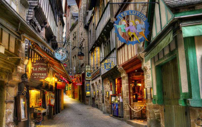 Calle adoquinada llena de pintorescas tiendas en edificios antiguos en la isla de Mont Saint-Michel
