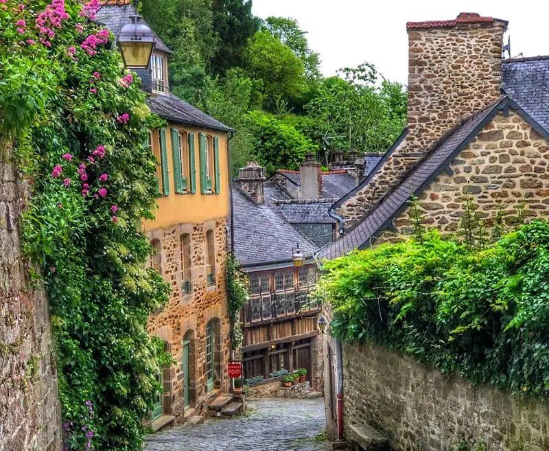 Calle empedrada empinada bordeada de antiguas casas de piedra cuyas paredes están cubiertas de enredaderas y rosas en flor