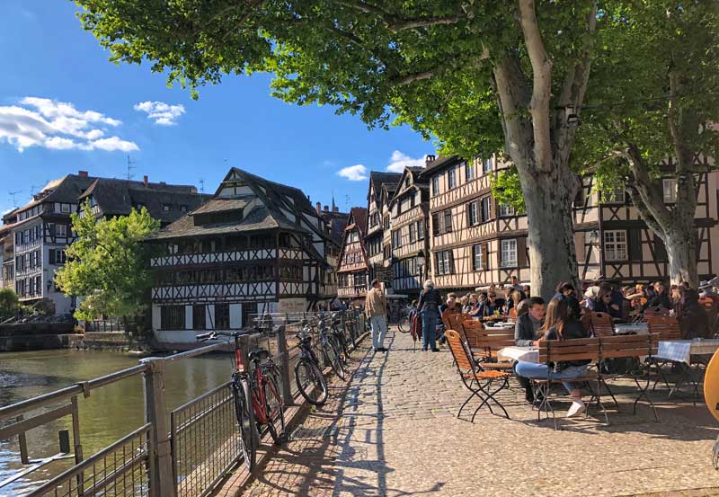 Casas con entramados de madera y cafés al aire libre bordean las orillas de un río en el distrito de Petite France Estrasburgo
