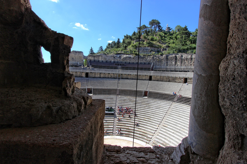 Teatro romano naranja visto desde lo alto de la muralla, detrás de la estatua de César 