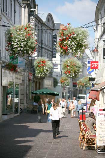 Calles llenas de cestas de flores en Cognac, mesas y sillas de café en calles empedradas