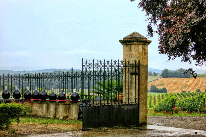 Tarros de Armagnac sobre un muro de piedra, como telón de fondo de campos y viñedos, Gers, Francia