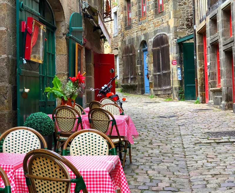 Mesas cubiertas con paños de cuadros rojos y blancos fuera de un restaurante en una calle adoquinada en Dinan