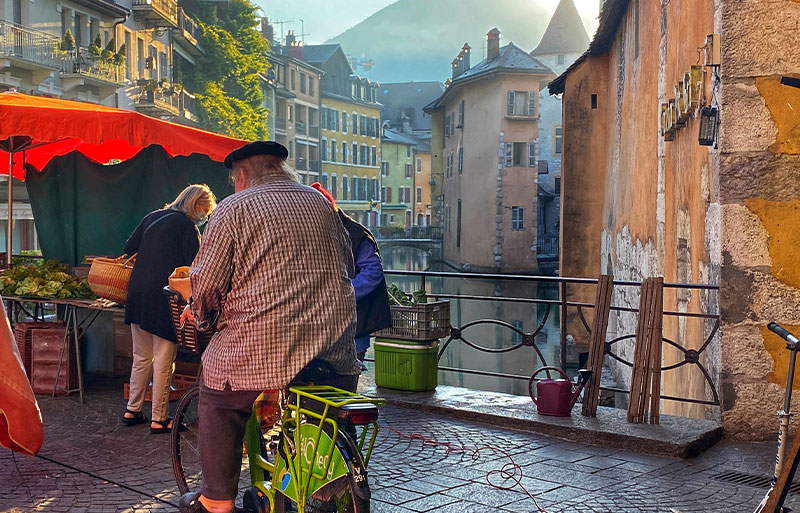 Hombre que llevaba una boina, andando en bicicleta a través de un puente adoquinado en Annecy