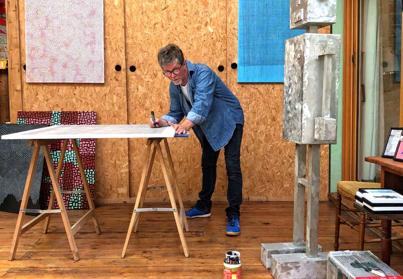Artista trabajando en un estudio en Le Havre inclinado sobre una mesa de trabajo, arte en las paredes