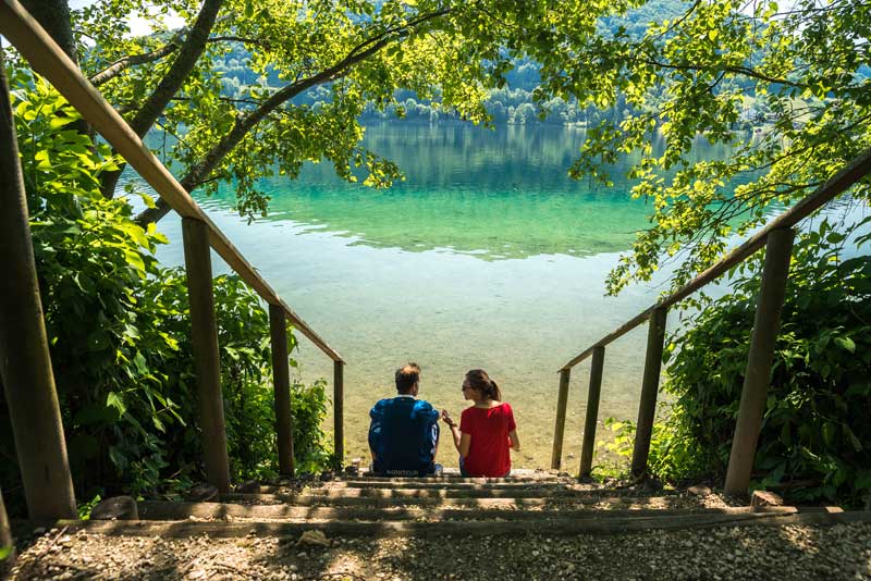 Un hombre y una mujer se sientan mirando hacia un lago cristalino rodeado de bosque en Isere, este de Francia