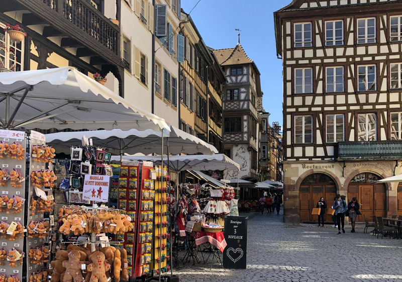 Calle adoquinada bordeada de edificios con entramado de madera que son tiendas y restaurantes, Estrasburgo