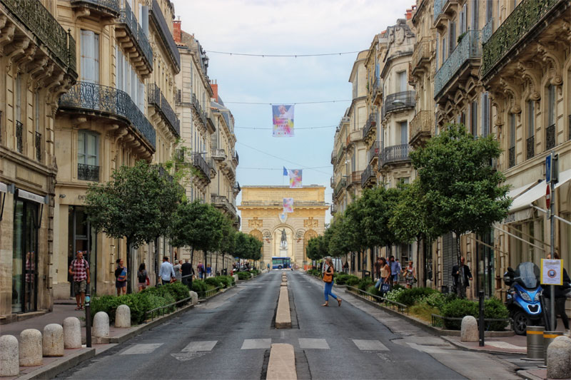 Promenade du Peyrou, Montpellier, una larga calle bordeada de edificios altos con un arco al final