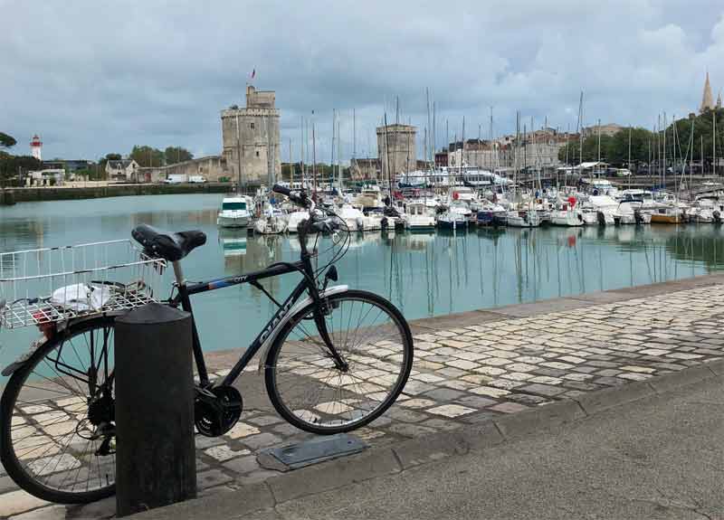 Bicicleta estacionada al lado del puerto de La Rochelle, el cielo nublado, el agua azul brillante