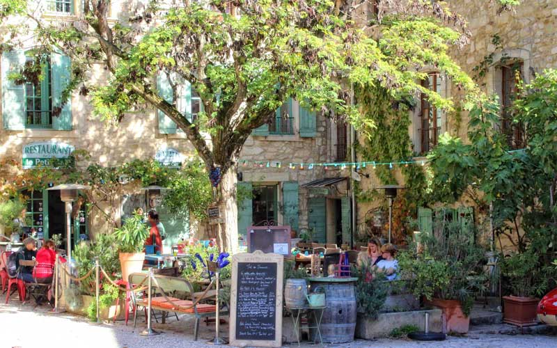 Gente sentada en una cafetería con terraza a la sombra de los árboles Oppede-le-Vieux, Provenza