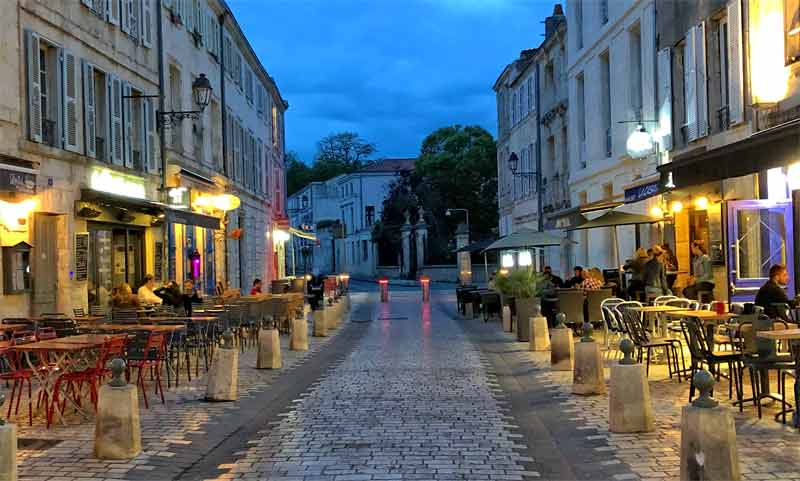 Calle adoquinada llena de restaurantes al atardecer en la Rochelle