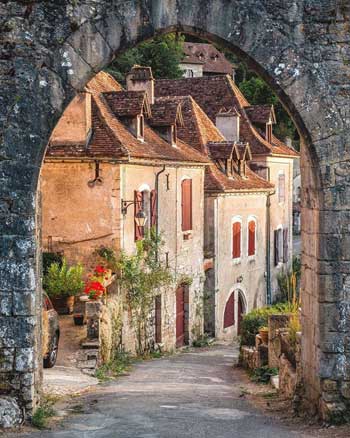 Vista a través de un arco de piedra de una calle adoquinada bordeada de casas antiguas, rosas trepando por las paredes