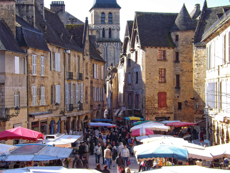 Plaza del mercado de Sarlat, Dordogne, coloridos toldos sobre los puestos, altos edificios medievales bordean la plaza