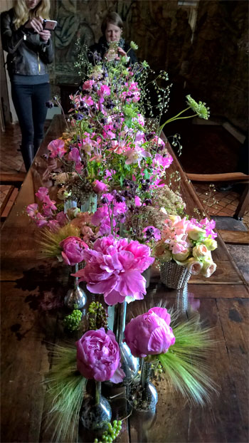 La gente toma fotografías con sus teléfonos móviles de una exquisita exhibición de flores sobre una mesa. 