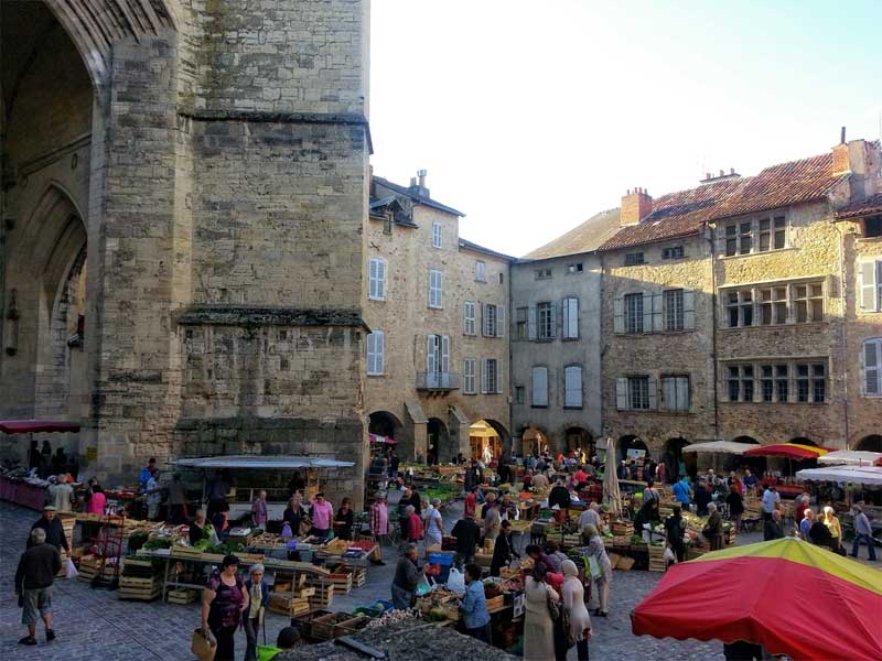 Mercado en una gran plaza adoquinada ante una imponente iglesia en Villefranche-de-Rouergue, Aveyron