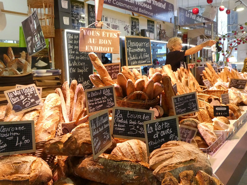 Mujer en un puesto de pan en el mercado de Saintes, Francia, con una gran variedad de panes