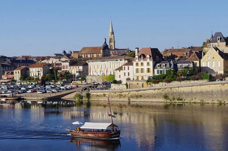 Vista de la ciudad de Bergerac, edificios como el muelle y un barco de recreo flota serenamente en el río