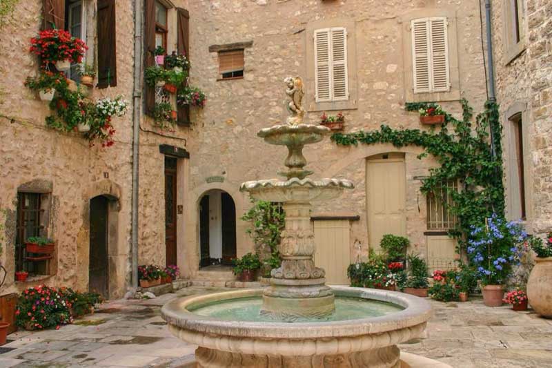 Bonita plaza con una fuente en el medio rodeada de antiguas casas de piedra.