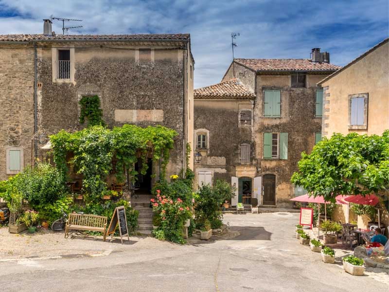 Antiguas casas de piedra con contraventanas en una pequeña plaza, un restaurante con sombrillas rojas, en el sur de Francia