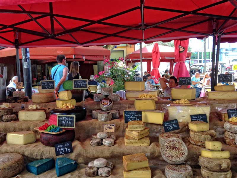 Puesto de quesos llenos de quesos franceses bajo un toldo rojo en el mercado de Carpentras