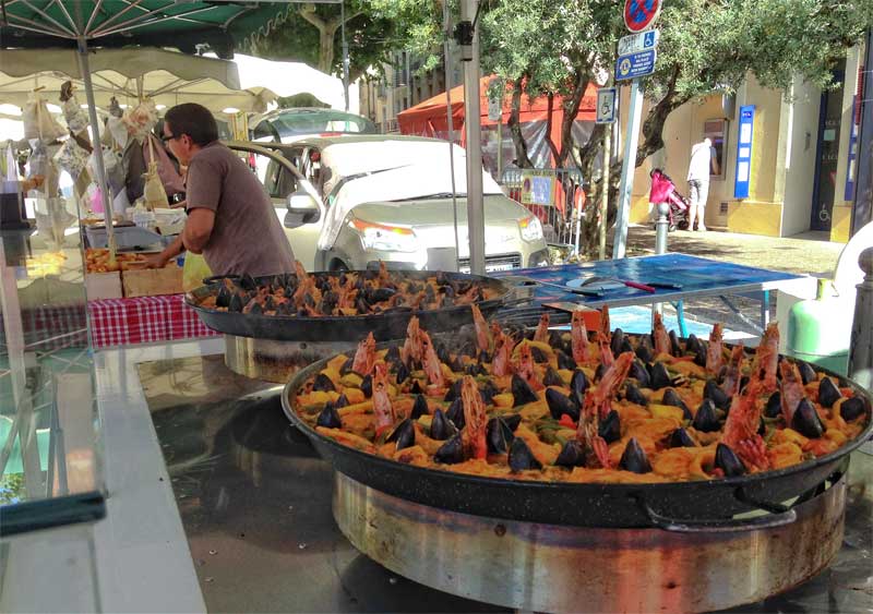 Comida callejera en el mercado de Carpentras, una gran cacerola de marisco y arroz bajo un toldo verde