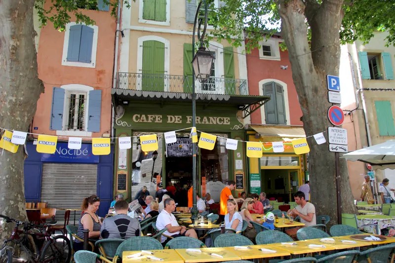 Gente sentada afuera de una cafetería en Francia, los plátanos dan sombra