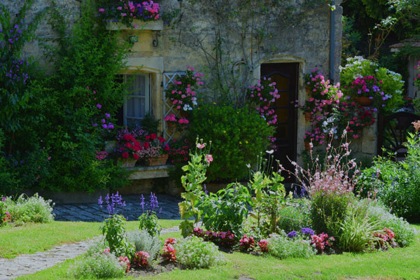 Fachada de una casa en blaye con flores en macetas, trepando por las paredes y el jardín