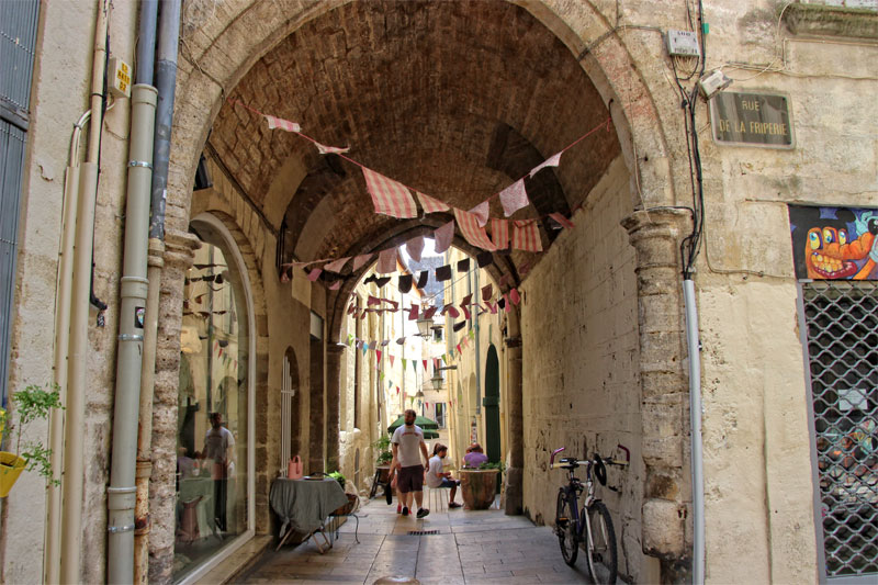 Banderines de rayas rosas y blancas cuelgan sobre una pasarela arqueada bordeada de edificios antiguos en Montpellier