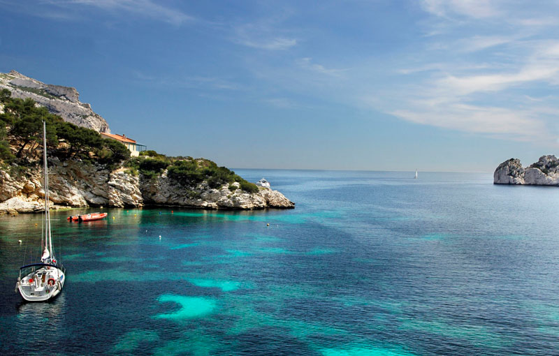 Una pequeña isla en las aguas verdes y azules del mar Mediterráneo, un pequeño barco se balancea hacia arriba y hacia abajo
