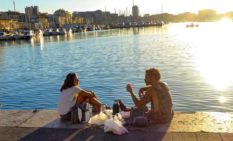 Un hombre y una mujer se sientan con un picnic en el muelle del antiguo puerto de Marsella al atardecer