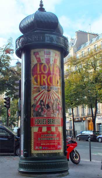 Columna publicitaria alta y verde, Morris Column, con un cartel de Folies Bergeres
