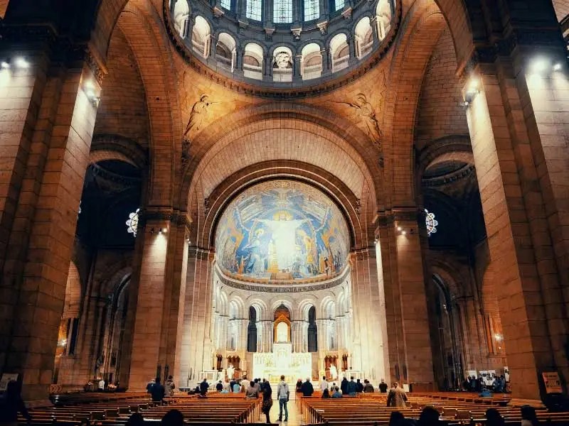 Interior de la iglesia del Sacre-Coeur de París, cúpulas llenas de luz y un enorme mosaico en el techo