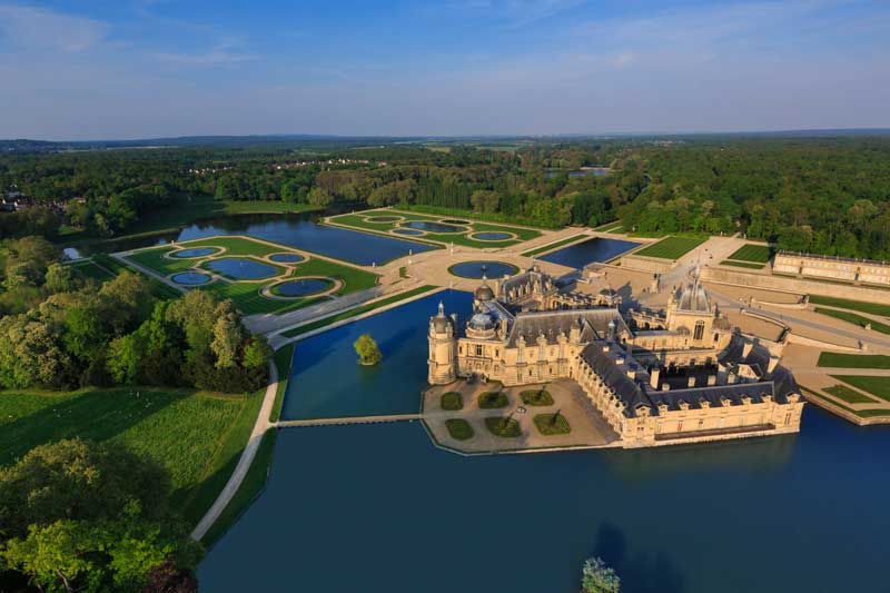 Vista aérea del Chateau de Chantilly que lo muestra rodeado de lagos y bosques.