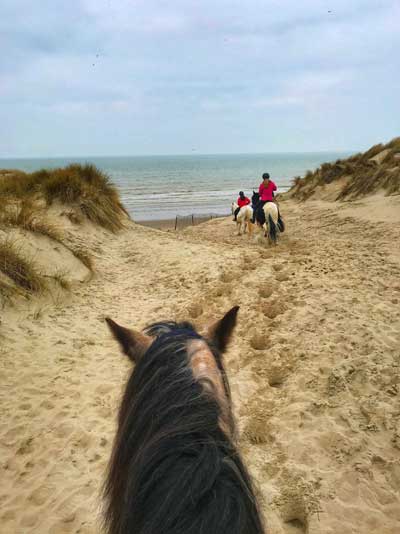 Gente a caballo en dunas de arena que conducen al mar en Le Touquet