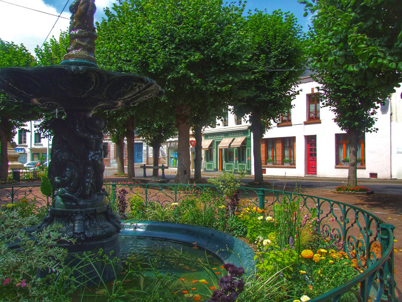 Hermosa fuente cubierta de flores en una tranquila plaza llena de tiendas de estilo antiguo, Montreuil-sur-Mer, Francia