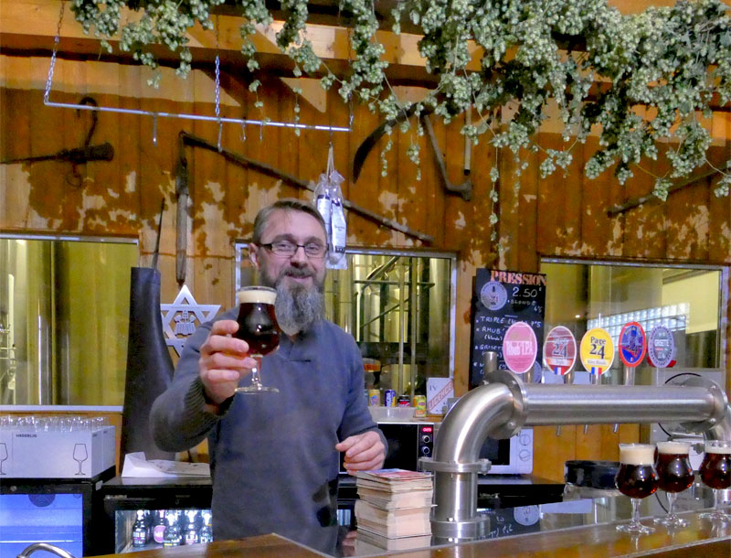 Un hombre sostiene una pinta de cerveza en una fábrica de cerveza artesanal en el norte de Francia, el lúpulo cuelga del techo