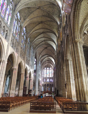 Nave de la iglesia de Saint Denis, París, techos muy altos, vidrieras que proyectan luz de colores sobre las paredes de piedra clara