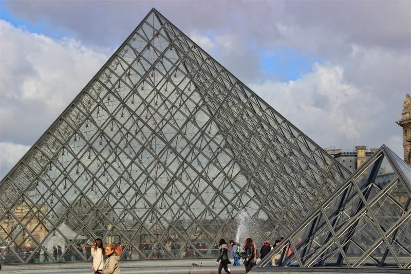 Entrada de la pirámide de cristal gigante al Louvre rodeada de cuencas de agua que se reflejan en el cristal.