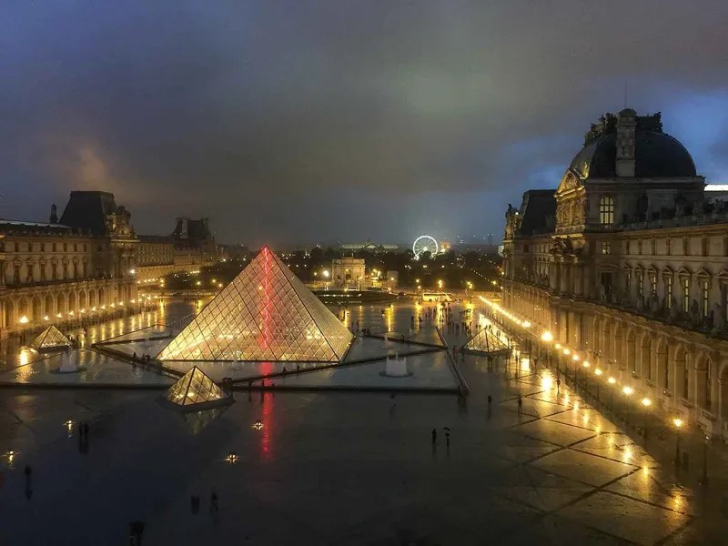 Entrada de la pirámide de cristal al Museo del Louvre en París por la noche, brillando suavemente en amarillo