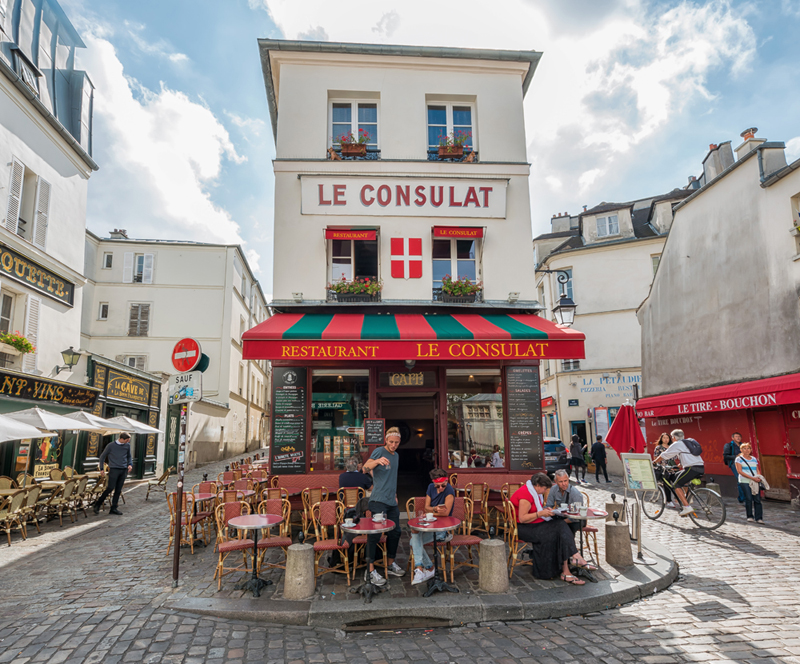 Famoso café en Montmartre París, Le Consulat en una calle adoquinada, la gente se sienta en mesas y sillas en la terraza