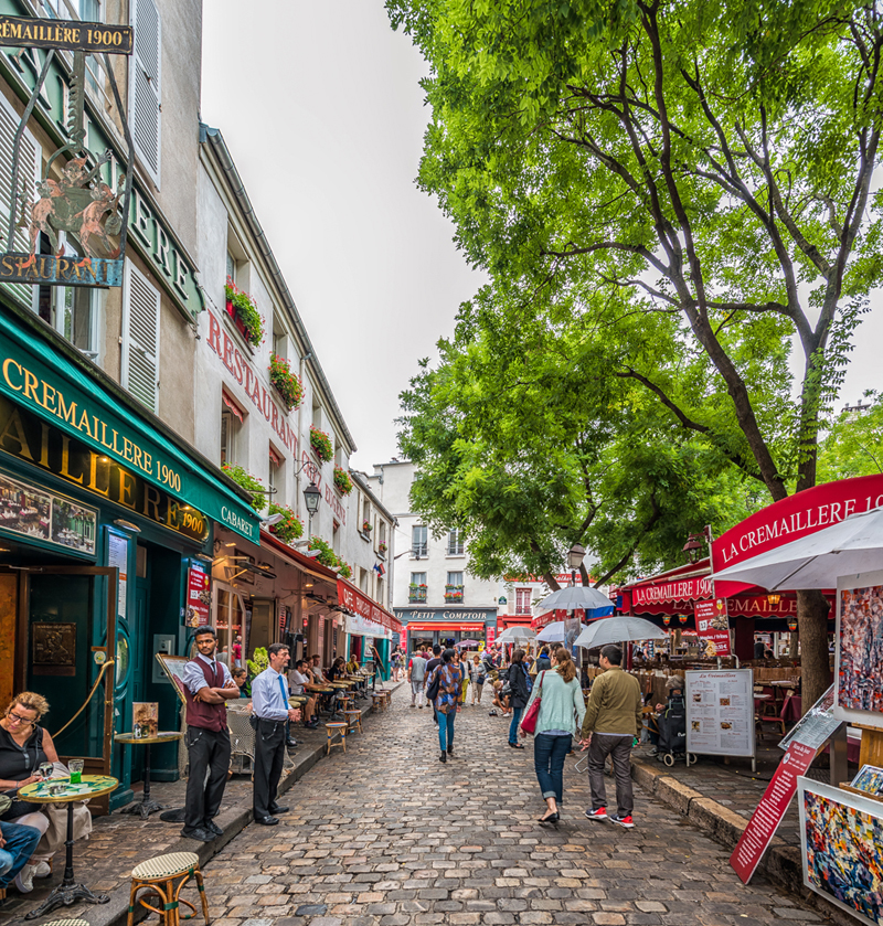 Calle adoquinada en Montmartre París, llena de coloridas tiendas y bares, árboles frondosos dominan las calles